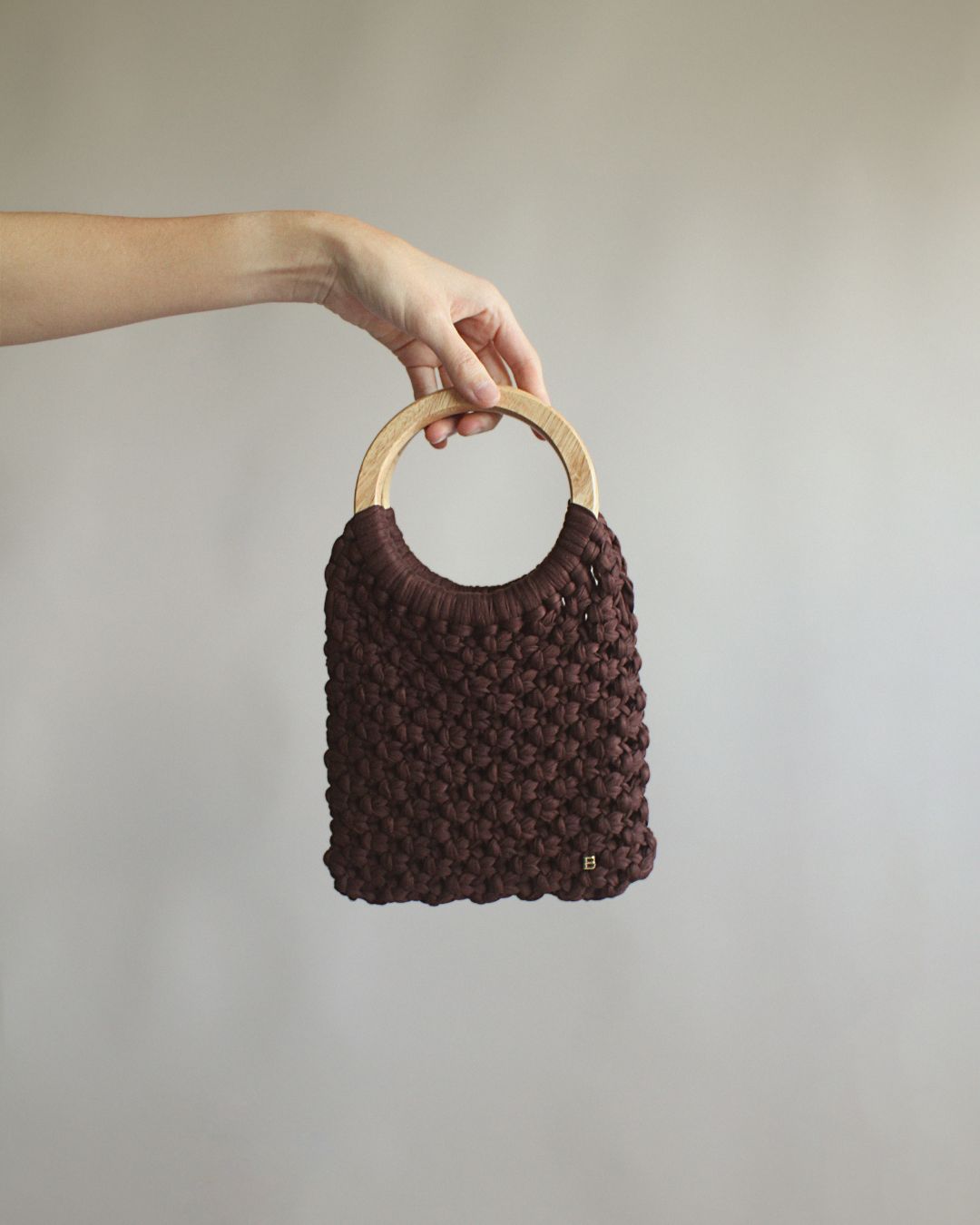 Gala Bag en color marrón, sujetado por las asas de madera. Vista frontal.