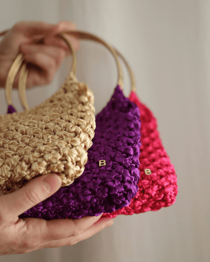 Roma Bag de color dorado, morado y fucsia. Vista en detalle de la B de Bimbú en la esquina inferior derecha. 